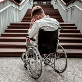 Depressed man on wheelchair worried on how to get up in the stairs.
